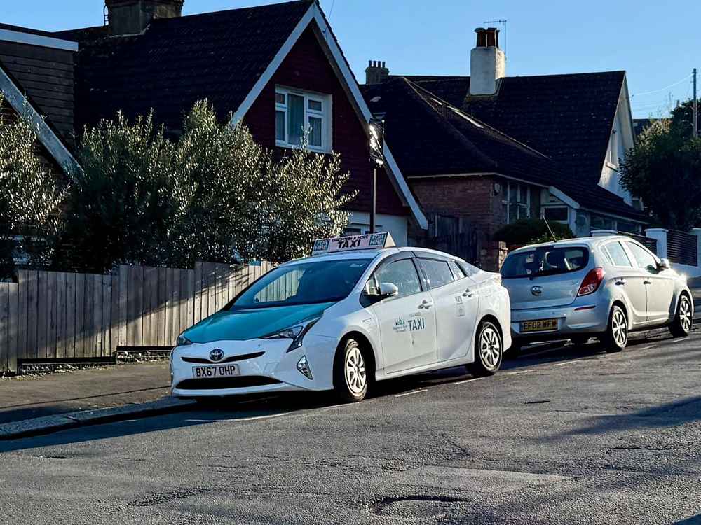 Photograph of BX67 OHP - a White Toyota Prius taxi parked in Hollingdean by a non-resident. The sixth of six photographs supplied by the residents of Hollingdean.