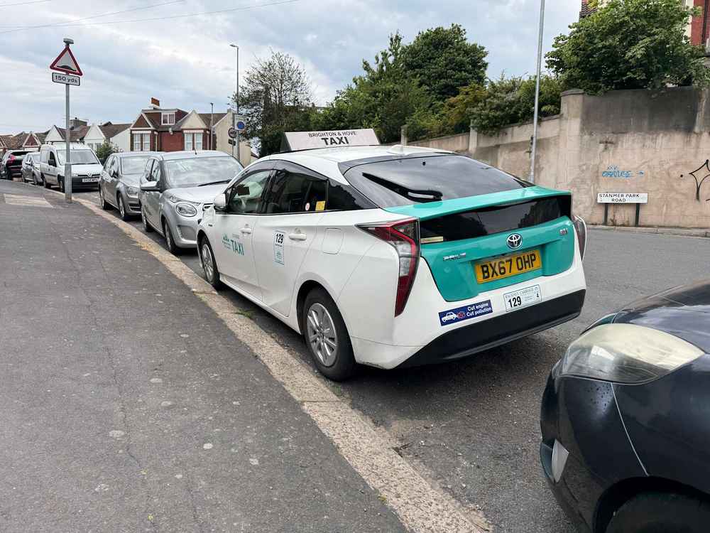 Photograph of BX67 OHP - a White Toyota Prius taxi parked in Hollingdean by a non-resident. The first of five photographs supplied by the residents of Hollingdean.