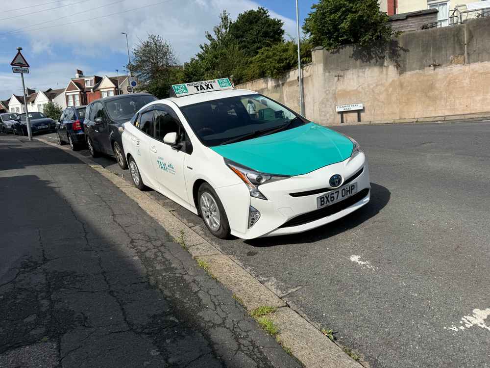 Photograph of BX67 OHP - a White Toyota Prius taxi parked in Hollingdean by a non-resident. The second of three photographs supplied by the residents of Hollingdean.