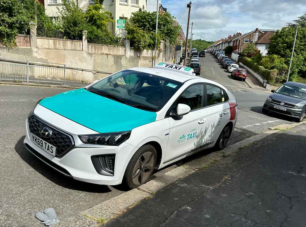 Photograph of YK69 TAS - a White Hyundai Ioniq taxi parked in Hollingdean by a non-resident. The first of six photographs supplied by the residents of Hollingdean.