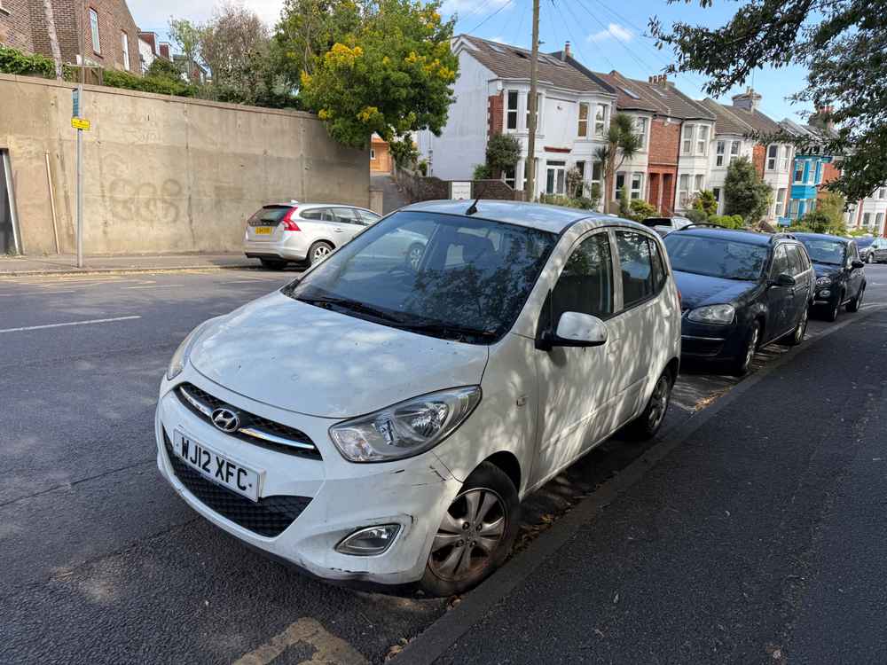 Photograph of WJ12 XFC - a White Hyundai i10 parked in Hollingdean by a non-resident, and potentially abandoned. The third of four photographs supplied by the residents of Hollingdean.