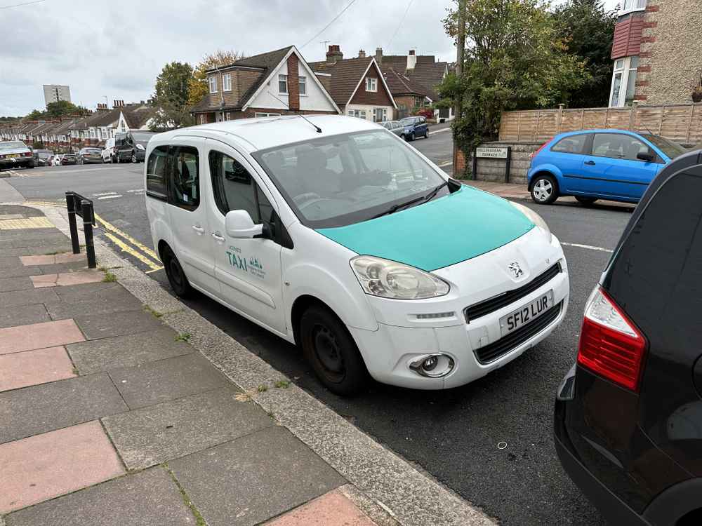 Photograph of SF12 LUR - a White Peugeot Partner taxi parked in Hollingdean by a non-resident, and potentially abandoned. The first of three photographs supplied by the residents of Hollingdean.