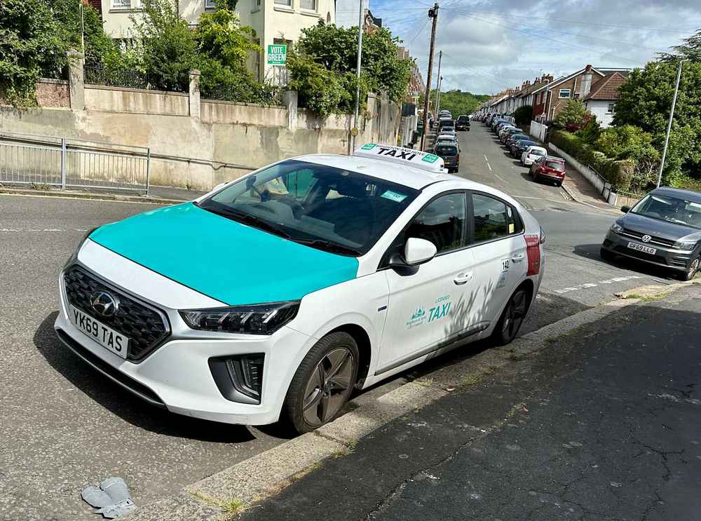 Photograph of YK69 TAS - a White Hyundai Ioniq taxi parked in Hollingdean by a non-resident. The first of fifteen photographs supplied by the residents of Hollingdean.